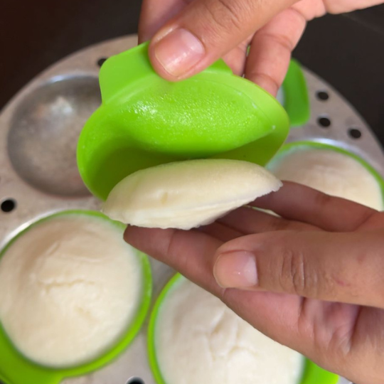 Idli batter being poured into green silicone liners